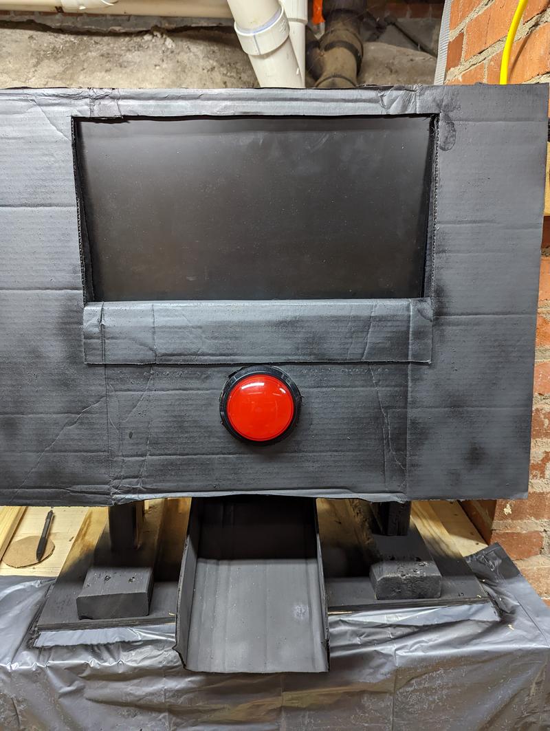 The front of the machine covered with a black piece of cardboard with cutouts for the button and the screen