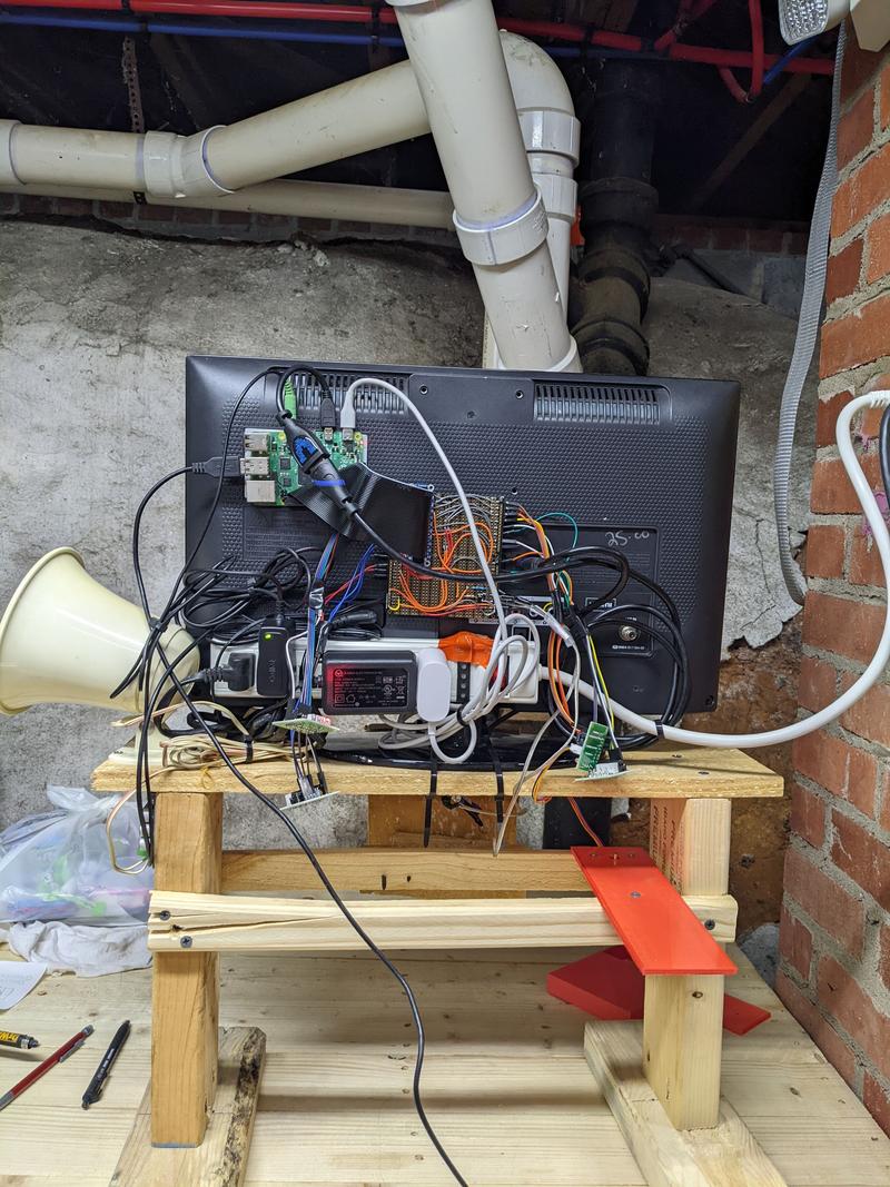 The jumble of wires and electronics glued to the back of a monitor that is mounted on a wooden stand